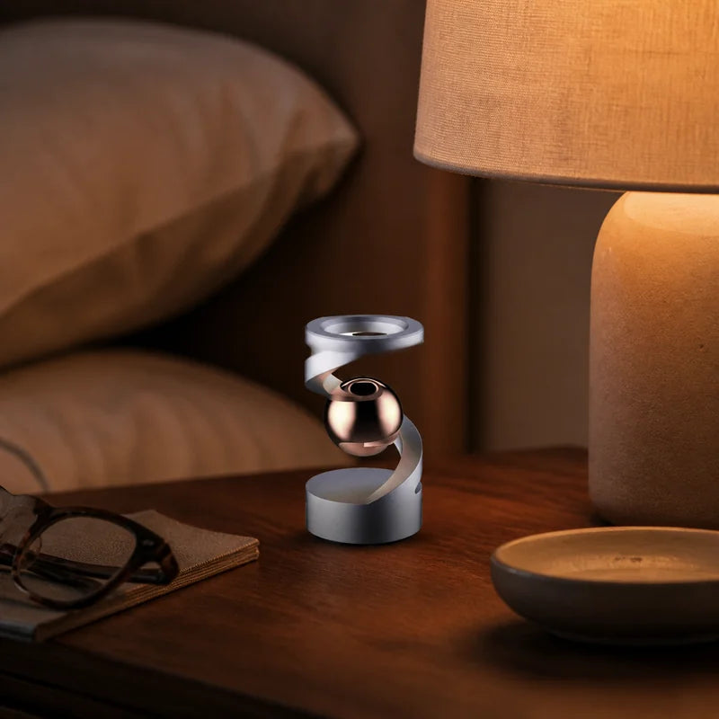 Gray Rose Gold levitation spinner on a bedside table beside a linen lamp at dusk